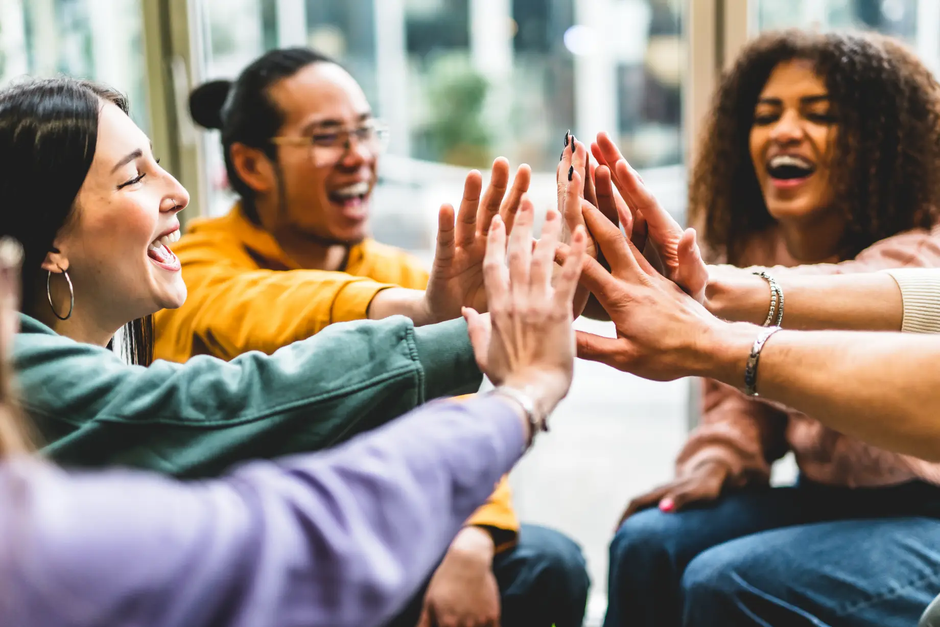 A diverse group of young adults, smiling and laughing, give each other a high-five in an Interpersonal Group Therapy at Transformation Health Services in Virginia Beach, VA
